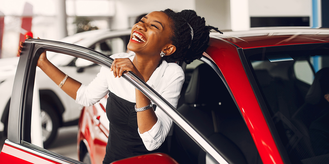 Photo of woman joyful and smiling getting out of a car at a car dealership.